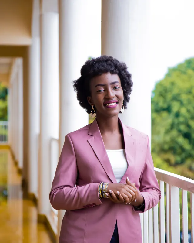 A smiling professional in a pink blazer standing in a bright corridor