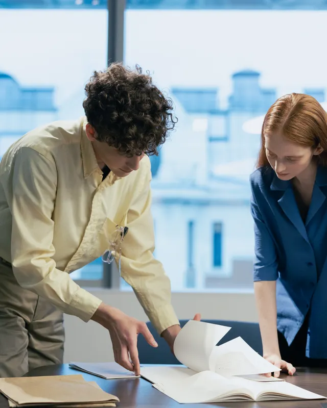 Two colleagues reviewing documents together at a desk by a window