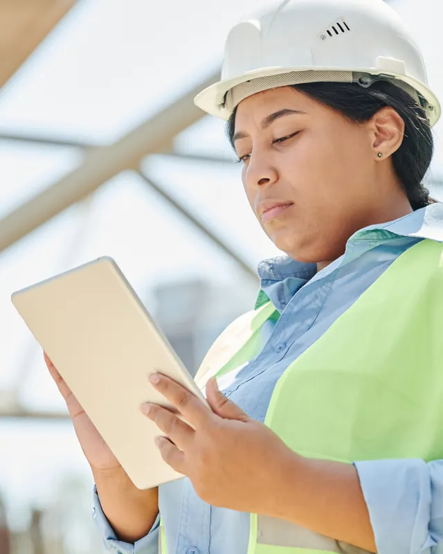 An engineer in a hard hat and high-visibility vest checking a tablet