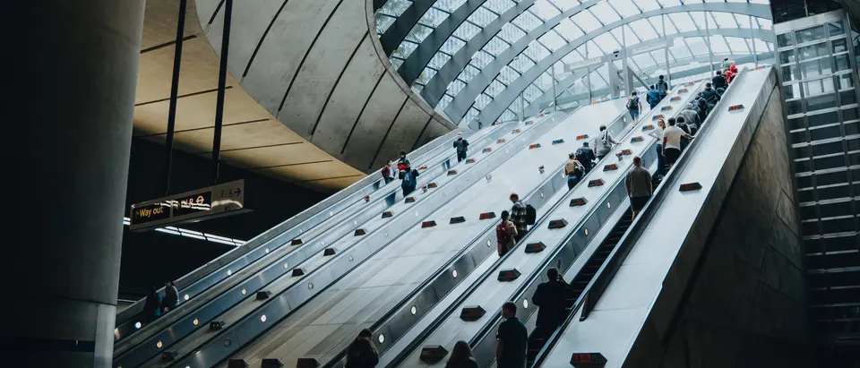 Commuters on long escalators inside a modern London Underground station
