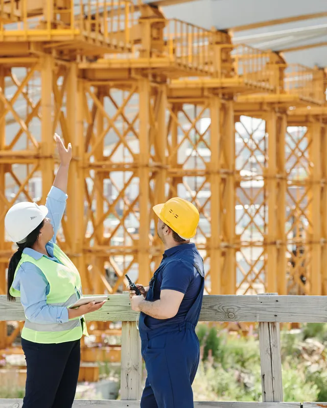 Two site workers in hard hats talking beside a timber structure