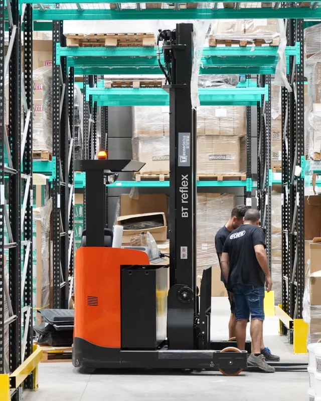 A warehouse worker beside a reach truck between tall racks of stock